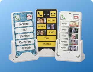 Three KISA Phones on cradles, each displaying high-contrast color screens with large buttons for easy access to contacts like family and essential services.